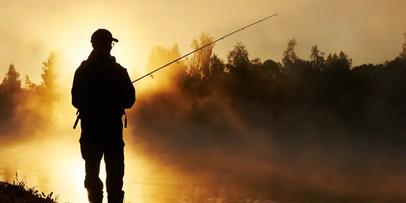 A man fishing from the shore of a lake.