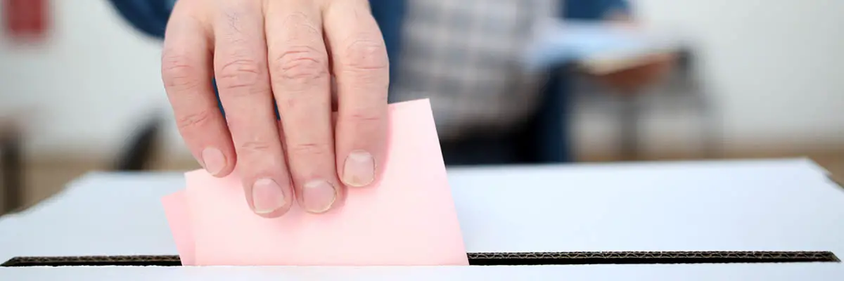 A hand placing a ballot in a box.